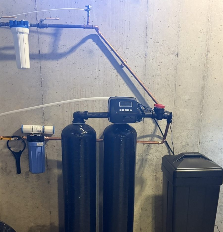 Twin-tank water softener with two pre-filters and copper plumbing on a basement wall